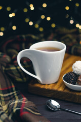 White cup of tea with spoon and chocolate candy on blurred background with christmas lights