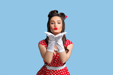 Lovely young pinup lady in stylish retro dress and bright makeup blowing air kiss at camera over...