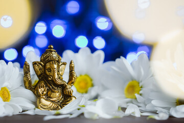 Golden lord ganesha sculpture in daisy flowers over blue illuminated background. Celebrate lord ganesha festival