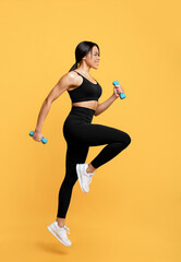 Fototapeta na wymiar Workout concept. Full length shot of young black woman in sportswear exercising with two dumbbells, yellow background