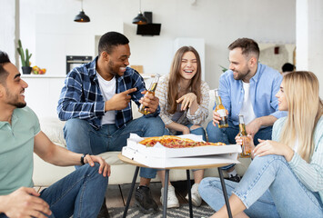 Fototapeta na wymiar Group of diverse male and female friends eating pizza at home, drinking beer, having conversation on student party