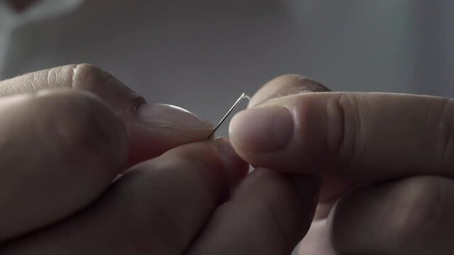A man is threading a sewing needle through the eye. The tailor sews clothes.