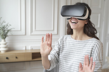 Young excited woman wearing VR headset interacting with augmented world, playing games at home