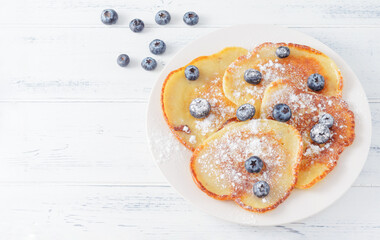 pancakes with blue blueberries and powdered sugar on a plate on a white wooden background