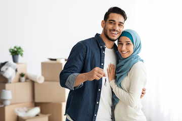 Happy muslim family standing over paper boxes and showing keys