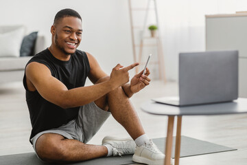 Black Fitness Guy Showing Smartphone To Laptop Recommending Application Indoor