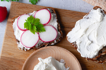 Home made rye bread on a wooden cutting board with curd cheese, radish and ricotta and herbs