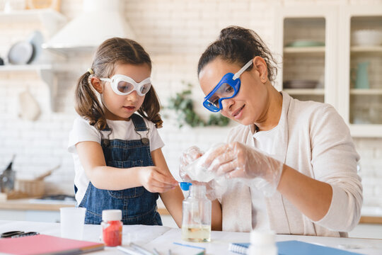 Scientific experiment at home. Laboratory tests for school homework. Parent mother with daughter kid making chemical test at home kitchen. Nanny babysitter teacher help in protective glasses