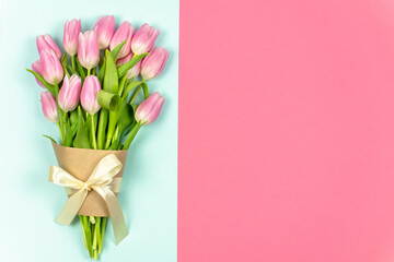 A bouquet of pale pink tulips tied with a ribbon and craft paper on a blue background. Pink background for text or logo. Copy space. Spring flowers. Valentine's Day, Easter