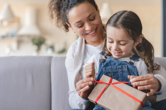 Mother And Little Daughter Girl Unwrapping Unpacking Birthday Christmas Mother`s Day Present Gift Box On Family Celebration Event At Home