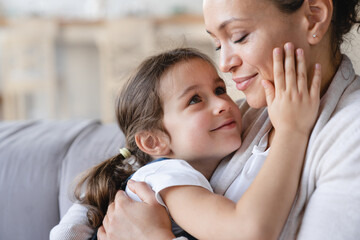 Girl looking at her mom. Young mother kissing hugging embracing her small little daughter. Motherhood, parenthood, love and family care concept. Happy Mother`s day!