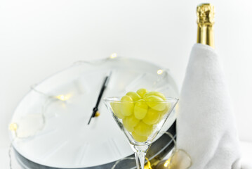 Wine glass with grapes on the background of a blurry clock and a bottle of champagne. Spanish...