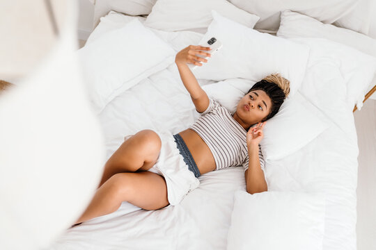 Young black woman taking selfie photo on cellphone while lying on bed