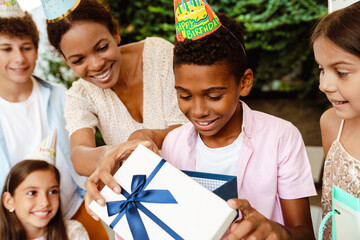 Black boy smiling while opening gift box during birthday party