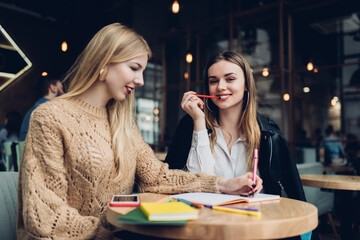 Positive young women sitting and studying in cafe together