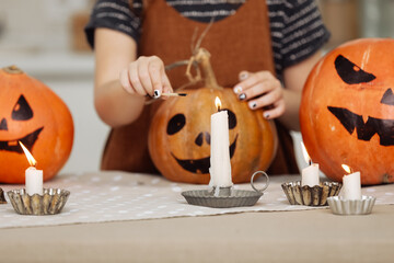 child girl lights a candle for Halloween. little girl in witch costume with carving pumpkin with a face made by child. Happy family preparing for Halloween. selective focus