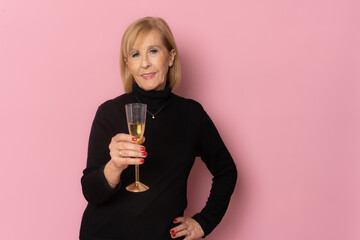 Smiling mature woman drinking champagne standing over pink background. Celebration concept.