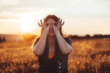 Happy smiling female in summer dress looks at the camera with her finger at a sunset