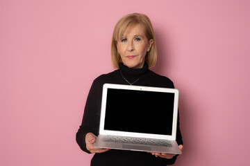 Naklejka premium Senior woman showing laptop computer screen isolated over pink background.