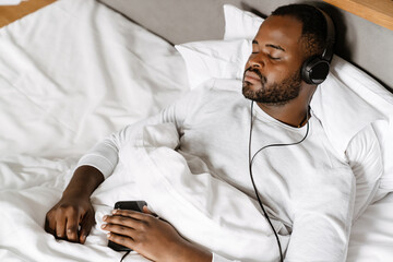 Black bristle man listening music while sleeping in bed