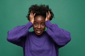 Fototapeta na wymiar One beautiful girl holding her head with arms isolated on dark green studio background. Afro hairdo. Concept of emotions, facial expressions