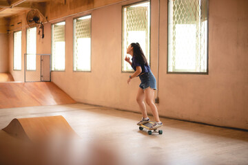 skateboard sport lifestyle, young Asian skater woman having fun with a board in a gym