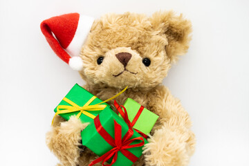 A stuffed toy Teddy bear in a red Santa Claus hat with a pompom on one ear, holding green gift boxes in its paws. White background. The concept of Christmas gifts, sales