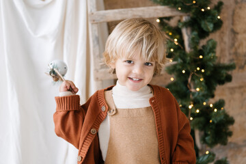 Caucasian blonde child portrait smiling and holding jingle bells while is listening to Christmas...