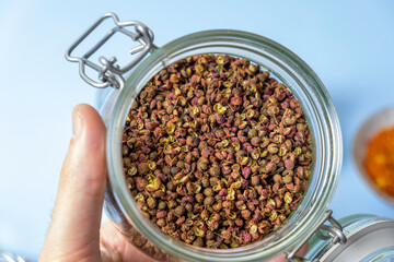 Close-up, a man holding a jar with dry useful herb for brewing. A jar of various herbs. Herbal tea. Sichuan papper
