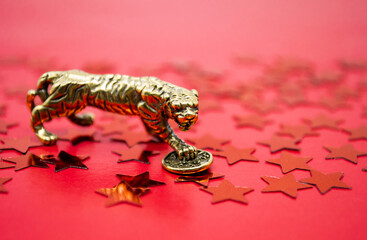 A bronze figure of a tiger with a coin on a background of red stars, a copy space