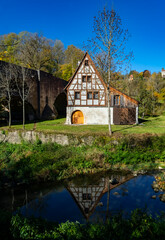 Fototapeta na wymiar Historic truss house at River Tauber in the Tauber valley in Rothenburg ob der Tauber Bavaria Germany. Sunny autumn atmosphere with arches of medieval bridge and water mirroring half timbered facade.