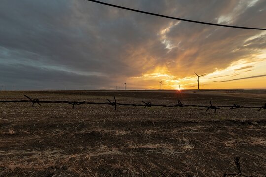 Countryside landscape at sunset with barbed wire in the foreground and wind turbines in the background