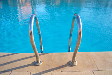 Close up of swimming pool stainless steel handrail descending into tortoise clear pool water....