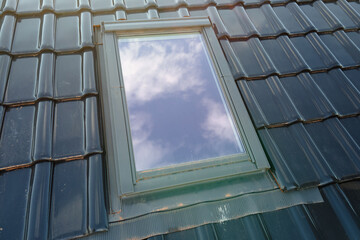 Closeup of attic window on house roof top covered with ceramic shingles. Tiled covering of building