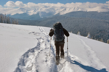 Man backpacker hiking snowy mountain hillside on cold winter day