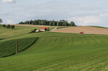 Valley with fields, a house and a red tractor in a village.