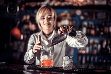 Pretty woman bartender intensely finishes his creation while standing near the bar counter in nightclub