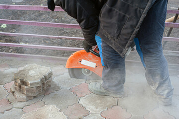 A worker cuts paving slabs with a gas cutter and a hand saw