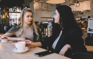 Positive friends chatting and having cup of coffee in cafeteria