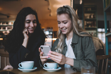 Happy multiethnic women using smartphone in cafe