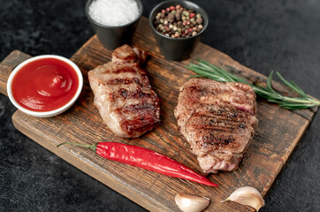 two grilled beef steaks with spices on a stone background
