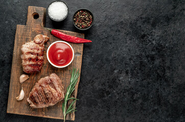 two grilled beef steaks with spices on a stone background with copy space	