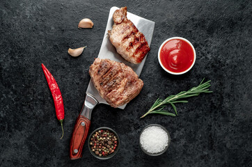 two grilled beef steaks with spices on a stone background