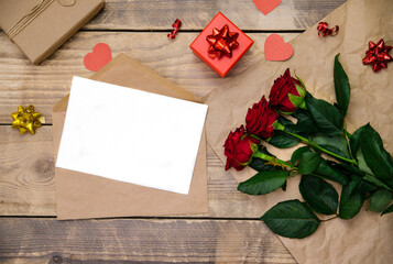 Naklejka na ściany i meble Top view, an envelope with an invitation or a postcard. Festive atmosphere, red roses, gift box on a wooden background.