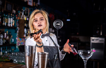 Experienced woman bartending pouring fresh alcoholic drink into the glasses at the night club
