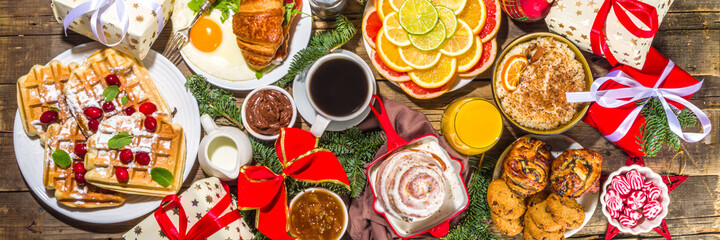 Festive Christmas morning breakfast or brunch table, with traditional foods – pancakes, Belgian waffles, fried eggs, croissant, stolen, cookies, with orange juice and coffee, cinnamon rice porridge 
