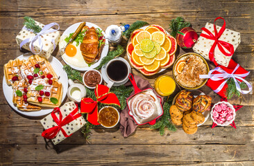Festive Christmas morning breakfast or brunch table, with traditional foods – pancakes, Belgian waffles, fried eggs, croissant, stolen, cookies, with orange juice and coffee, cinnamon rice porridge 