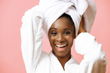 Young beautiful black woman in bathrobe with white towel on head posing on pink background