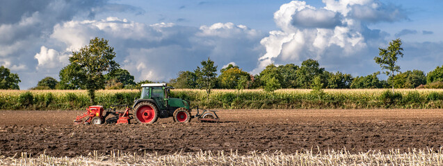 Rural panorama with cumulus clouds in the sky and a tractor in the field cultivating the farmland -...