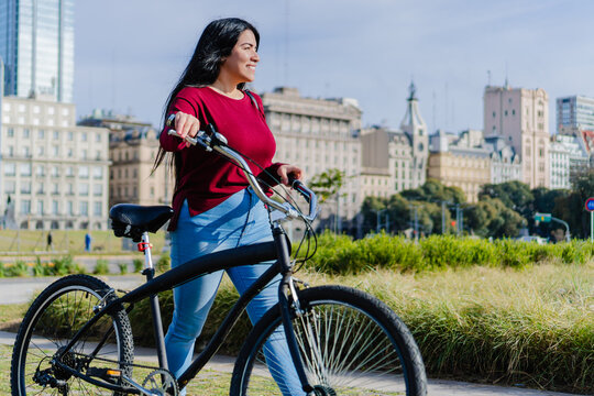 Young Latin Business Woman Walking Through The City On A Bicycle, Green Mobility